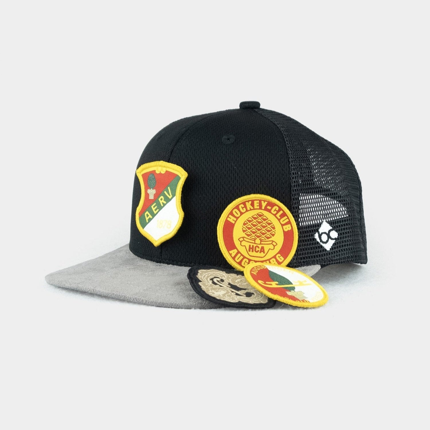 Schwarze Cap mir grauem Schirm. Daneben sind die auswechselbaren Retro-AEV-Patches zu sehen.