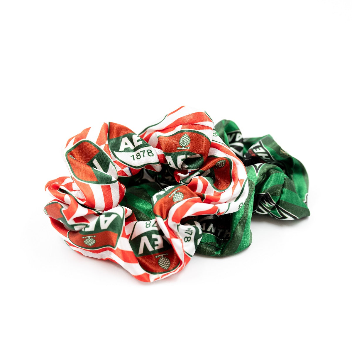 rot-weißer Haargummi mit AEV-Logo, unter diesem liegt ein grün gestreifter Haargummi mit Pantherlogo